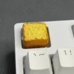 Adorable artisan toast keycap, a unique miniature food-inspired design. Showcases its warm, cozy, handcrafted aesthetic, perfect for mechanical keyboard.