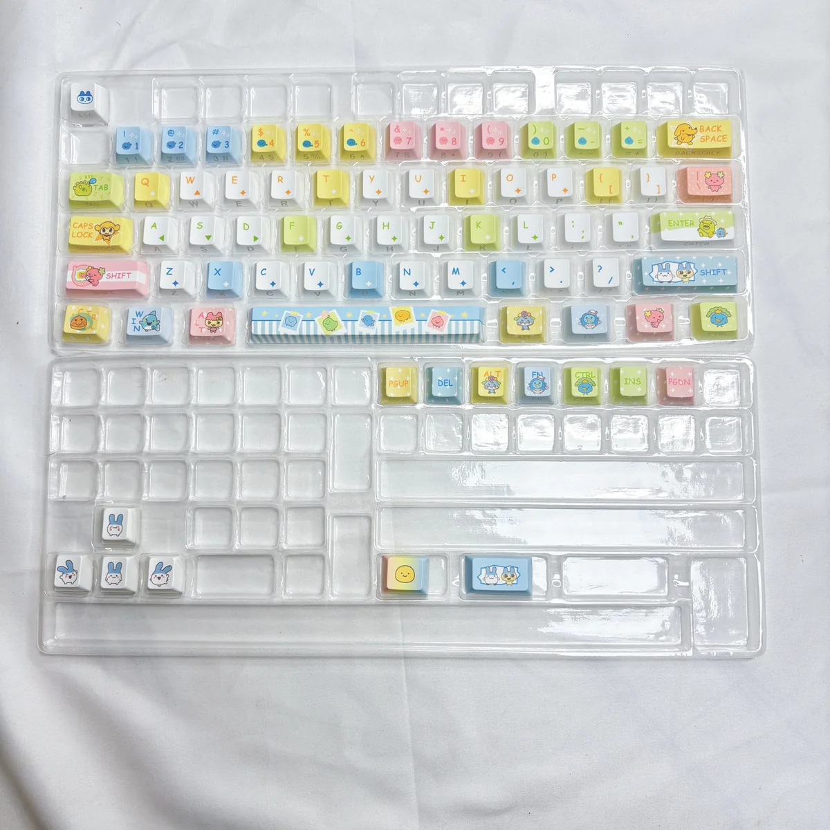 A collection of vibrant Tamagotchi Keycaps, showcasing pixelated retro digital pet designs on durable PBT from various playful angles.