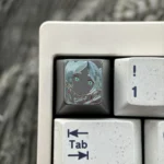 Artistic hand-carved Frieren titanium artisan keycap from a unique angle, revealing the detailed silhouette and fine lines on its colored matte surface.