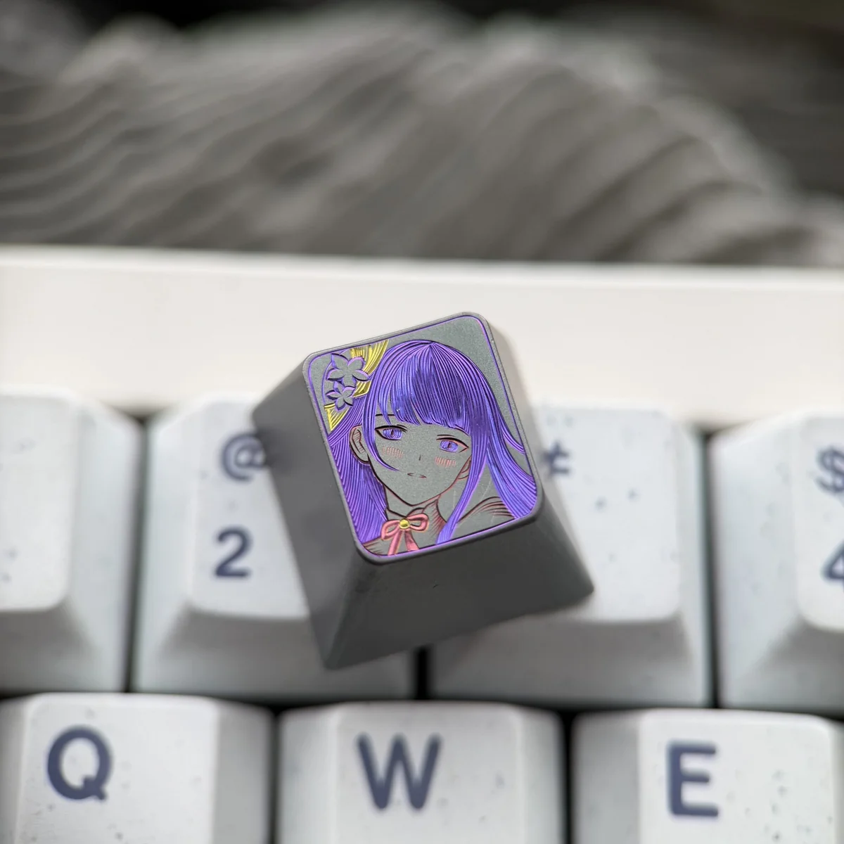 Hand-carved Raiden Shogun titanium artisan keycap from a unique angle, highlighting intricate lines and matte finish.