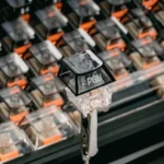 Glossy black gradient PC keycap with side-lit PGU legend and frosty ink fade, mounted on a switch against a mechanical keyboard.