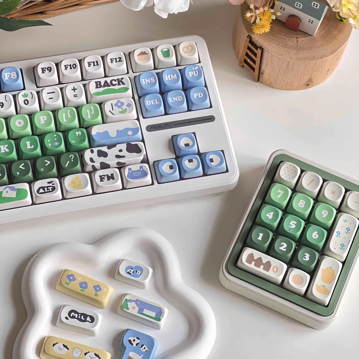 Cow pasture keycaps MOA PBT dye-sub set shown on a keyboard and matching number pad, with cream cows, green meadows, blue sky, and milk accents.