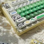 Close-up of cow pasture keycaps on a keyboard, featuring green meadow letters, cream cow spots, and playful milk accents on dye-sub PBT MOA keys.