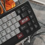 Angled close-up of the Drift Keycap Set, showing white alphas, black modifiers, and red JDM car novelties on ABS double-shot keycaps.