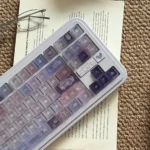 Frosted floral keycaps on a pastel purple and pink PC keyboard set with delicate floral illustrations in soft light.