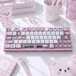 Pastel pink gloomy bear keycaps with PBT side-engraved translucent designs, shown on a sweet desk with lace, hearts, and cute accessories.