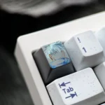 Close-up of a hand-carved titanium Gojo Satoru keycap with blue accents mounted on a white mechanical keyboard.