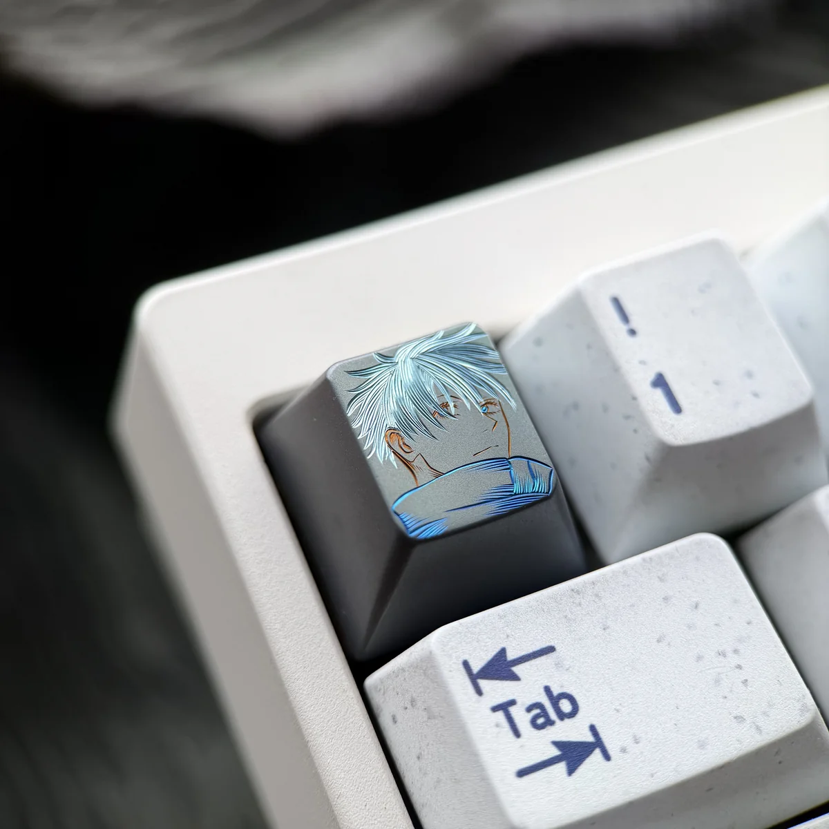 Close-up of a hand-carved titanium Gojo Satoru keycap with blue accents mounted on a white mechanical keyboard.