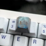 Hand-carved titanium Gojo Satoru keycap mounted on a white keyboard, featuring a monochrome portrait with vivid blue accents.