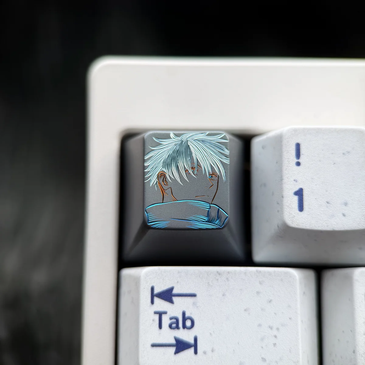 Hand-carved titanium Gojo Satoru keycap with a monochrome portrait and vivid blue accents on dark metal, shown on a keyboard.