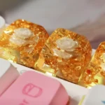 Handcrafted 3D camellia artisan resin keycap, SA profile, viewed from an artistic angle, highlighting delicate blooms and shimmering metallic foil from an artistic angle.