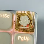 Artistic handcrafted 3D Camellia artisan resin keycap, SA profile. Delicate bloom encased in clear resin with shimmering metallic foil accents.