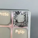 Handcrafted artisan resin keycap featuring a delicate white 3D camellia bloom encased in clear resin with shimmering gold foil accents, SA profile.