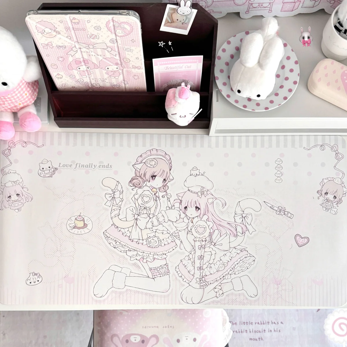This pastel pink kawaii anime desk mat shows lolita cat-girl line art with ribbons, hearts and polka dots on oversized waterproof non-slip PU.