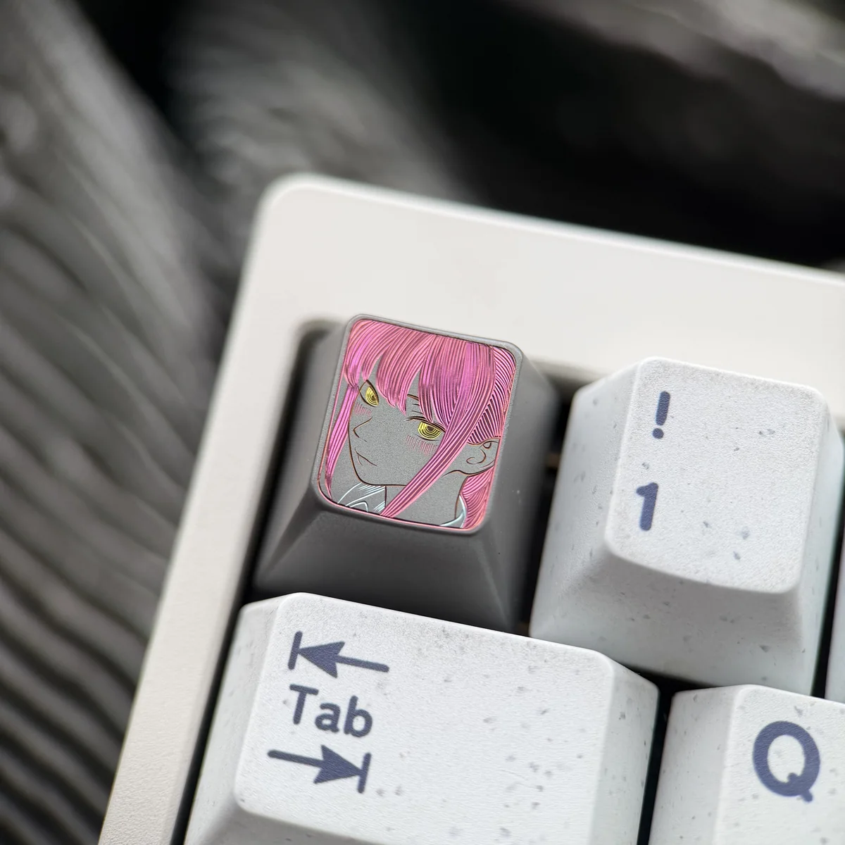 Hand-carved titanium Makima artisan keycap, shown from a unique angle. Highlights intricate line art and dark metallic finish.