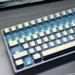 This close-up angled view shows translucent blue keycaps with pearlescent PBT/PC shine-through, floral vine engravings and luminous ice-blue glow.