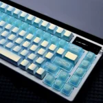 Angled view of translucent blue keycaps showing pearlescent ice-blue shine-through, delicate floral vine engravings, and a soft luminous gradient.