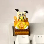 Ultra-detailed 3D Pokemon artisan keycap featuring a dessert-themed Cosplay Pikachu in a Mimikyu hood, holding an orange slice on a cake base.