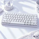 Angled white Polar Bear keycaps PC MOA 139-key set with bear novelty keys beside a snowy polar bear snow globe on a winter desk.