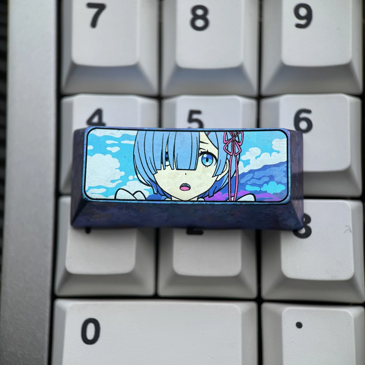 Rem titanium keycap on a keyboard reveals anodized titanium finish, artisan blue anime portrait, and dreamy iridescent sky tones.