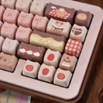 This close-up shows pastel pink and chocolate brown dye-sublimated PBT MOA Strawberry Chocolate keycaps with strawberry cake and gingham motifs.