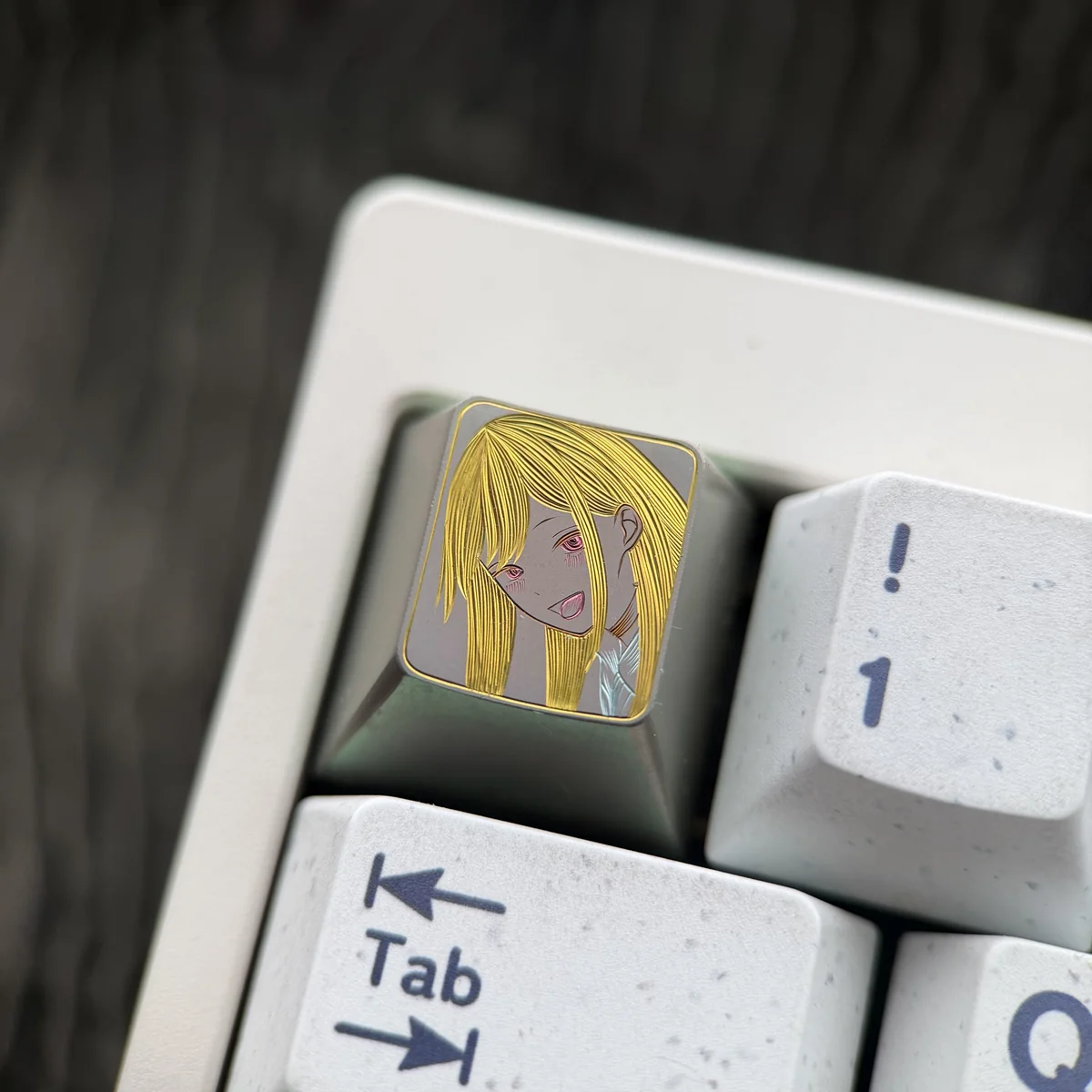Close-up of a hand-carved titanium anime keycap featuring Marin Kitagawa's blonde portrait with golden linework on a muted titanium surface.
