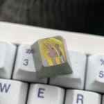 Angled view of the hand-carved titanium anime keycap featuring the blonde Marin Kitagawa portrait in golden linework on muted titanium.
