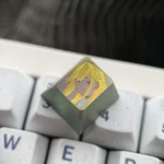 Hand-carved titanium anime keycap featuring a golden linework portrait of Marin Kitagawa, shown at an angled view on a white keyboard.